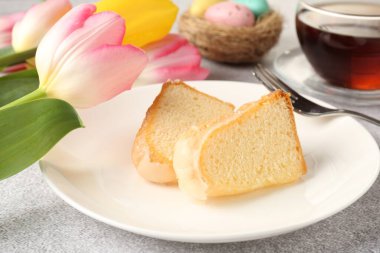 Lezzetli kek parçaları, Paskalya yumurtaları, laleler ve çay gri masada, yakın plan.