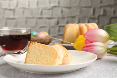 Lezzetli kek parçaları, Paskalya yumurtaları, laleler ve çay gri masada, yakın plan.