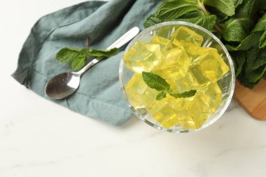 Tatlı kâsesinde sarı jöle küpleri ve beyaz mermer masada nane şekeri.