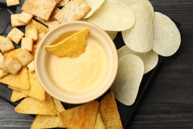 Lezzetli peynir sosu kaseye ve farklı aperatifler, koyu ahşap masa, üst manzara.