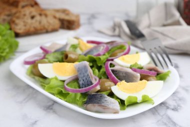 Ringa balıklı lezzetli salata, yumurta ve sebzeler beyaz mermer masada, yakın plan.