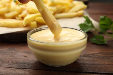Patates kızartmasını ahşap masada peynir sosuna batırmak, yakın plan.