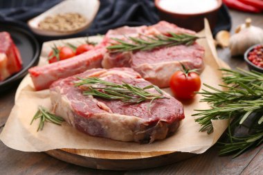 Çiğ et parçaları, biberiye ve domatesler ahşap masada, yakın plan.