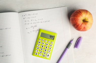 Ev ödevi. Matematik ödevli defter, beyaz masada elma ve kırtasiye malzemesi, düz konum