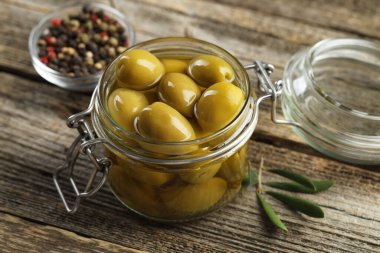 Cam kavanozda turşulu yeşil zeytin ve ahşap masada baharatlar, yakın plan.