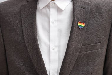 Kapalı alanda LGBT bayrağı renginde kalp şeklinde iğnesi olan adam, yakın plan