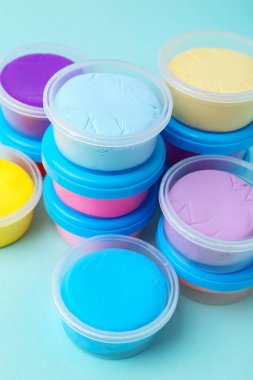 Açık mavi arka planda plastik kavanozlardaki farklı renkli modelleme killeri, yakın plan