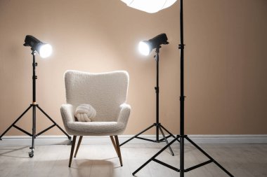 Profesyonel ışıklandırma ekipmanları ve fotoğraf stüdyosunda dekoratif yastıklı koltuk.