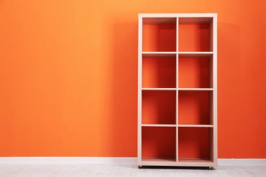 Turuncu duvarın yanındaki boş ahşap raf ünitesi.