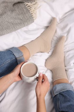 Bir fincan sıcak içecekle yatakta bej çorap giyen bir kadın.