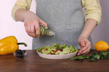 Beyaz arka plana karşı ahşap masada lezzetli salataya yağ döken kadın, yakın plan.