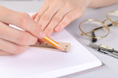 Beyaz masadaki deftere cetvel ve kalemle çizim yapan kadın, yakın plan.