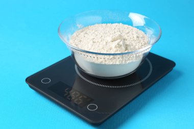 Açık mavi zemin üzerinde un bulunan elektronik mutfak terazisi, yakın plan.