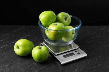 Elektronik mutfak terazisi, siyah arka planda koyu dokulu yeşil elma kasesi, yakın plan.