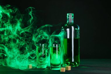 Absinthe shot bardakları, şişe ve esmer şeker siyah arka planda dumanlı