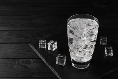 Soda bardakta tazeleniyor. Siyah tahta masada buz küpleri var. Metin için yer var.