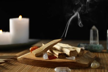 Smoldering palo santo stick, gemstones and burning candles on table, closeup
