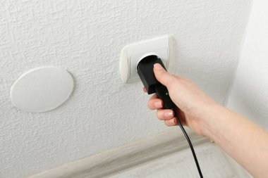 Kadın USB güç adaptörünü şarj kablosuyla kapalı mekandaki elektrik prizine takıyor.