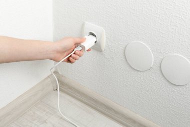 Kadın USB güç adaptörünü şarj kablosuyla kapalı mekandaki elektrik prizine takıyor.