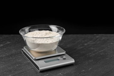 Elektronik mutfak terazisi ve koyu renkli bir kase un, siyah arka planda, yakın plan.