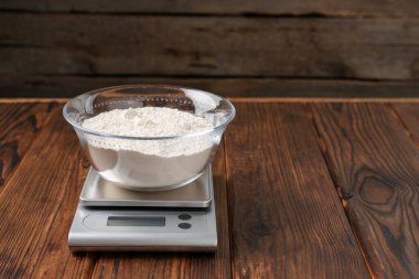 Elektronik mutfak terazisi ve ahşap masa üzerinde bir kase un. Metin için boşluk