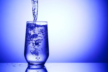 Serinletici gazoz suyunu mavi arka planda cama döküyorum, yakın plan. Metin için boşluk