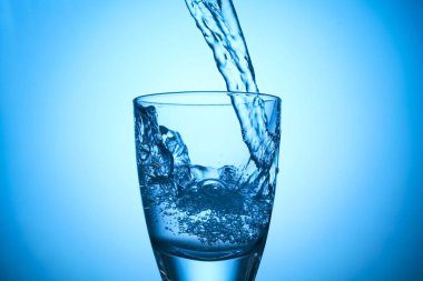 Pouring refreshing soda water into glass on light blue background, closeup