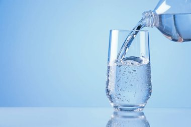 Açık mavi arka planda şişeden bardağa ferahlatıcı soda dökülüyor, yakın plan. Metin için boşluk