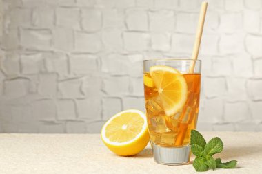 Buzlu çayı, saman, nane ve limon dilimleri ile serinleterek gri arkaplana karşı hafif desenli masada, yakın plan. Metin için boşluk