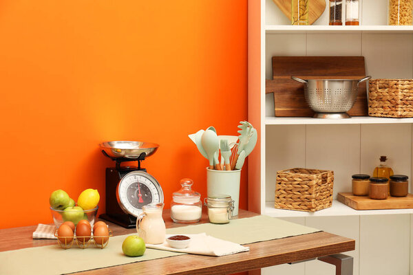 Kitchen scale, products and cooking utensils on wooden table. Space for text