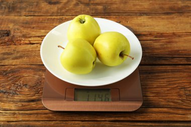 Modern electronic kitchen scale with apples on wooden table, closeup