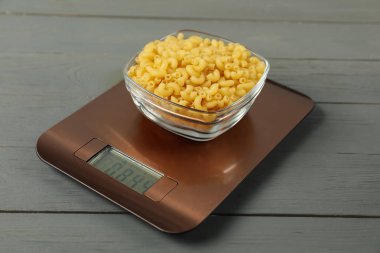 Modern elektronik mutfak terazisi. Gri ahşap masada çiğ makarna var. Yakın plan.