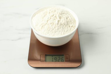 Modern elektronik mutfak terazisi, beyaz mermer masa üzerinde bir kase un, yakın plan.