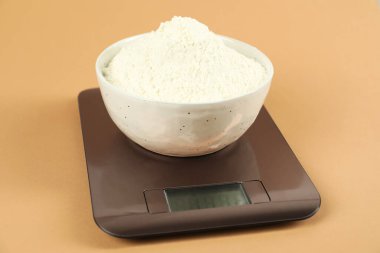 Elektronik mutfak terazisi, bej arka planda bir kase un, yakın plan.