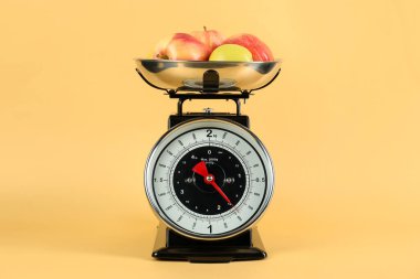Mechanical kitchen scale with bowl of apples on yellow background