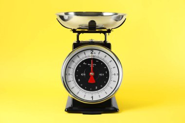Mechanical kitchen scale with bowl on yellow background, closeup