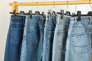 Many stylish jeans hanging from rack on white background, closeup