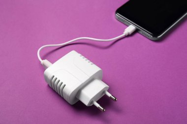 USB güç adaptörü mor arkaplandaki akıllı telefona bağlı şarj kablosu, yakın plan