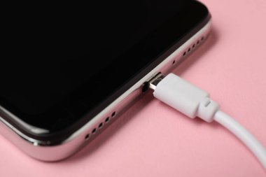 USB şarj kablosu soluk pembe arka planda akıllı telefona bağlı, yakın plan