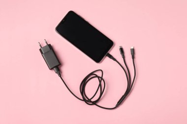 Soluk pembe arka planda akıllı telefona bağlı üç şarj kablosu, üst görünüm