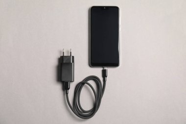 Açık gri arkaplanda şarj kablosu ve akıllı telefonu olan USB güç adaptörü, üst görünüm