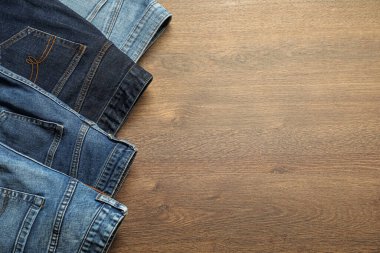 Different stylish jeans on wooden background, flat lay. Space for text