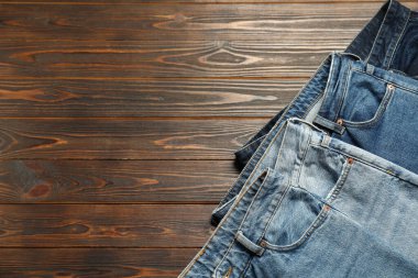 Different stylish jeans on wooden background, flat lay. Space for text
