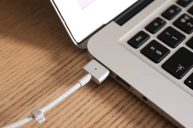 Tahta masadaki dizüstü bilgisayara bağlı şarj kablosu, yakın plan.