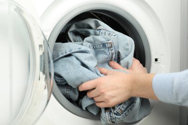 Kadın çamaşır makinesine kot pantolon koyuyor, yakın plan.
