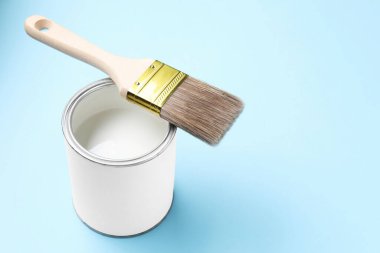 Açık mavi arka planda beyaz boya ve fırça kutusu, yakın plan. Metin için boşluk