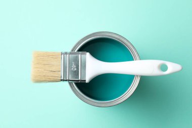 Can of bright paint and brush on turquoise background, top view