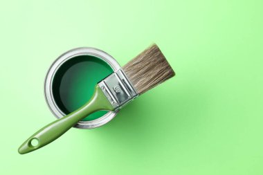 Can of bright paint and brush on light green background, top view