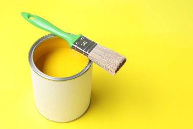 Can of bright paint and brush on yellow background, space for text