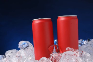 Refreshing drinks in cans on ice cubes against dark blue background